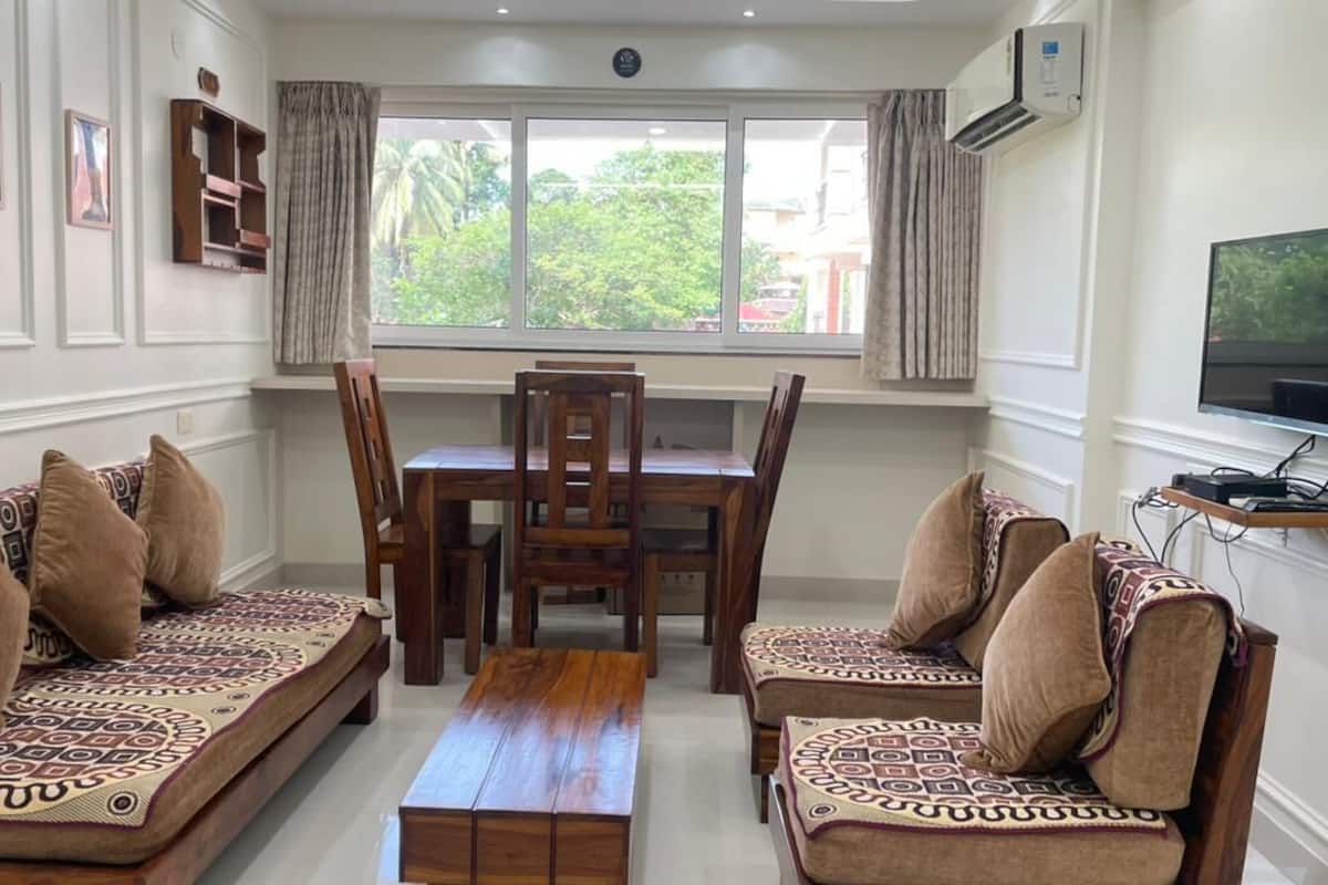 A living room with a wooden dining table, two sofas, and a TV on the wall.