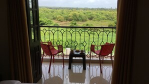 A balcony with a table and two chairs, overlooking a lush green landscape. - Monarch suites (Candolim)