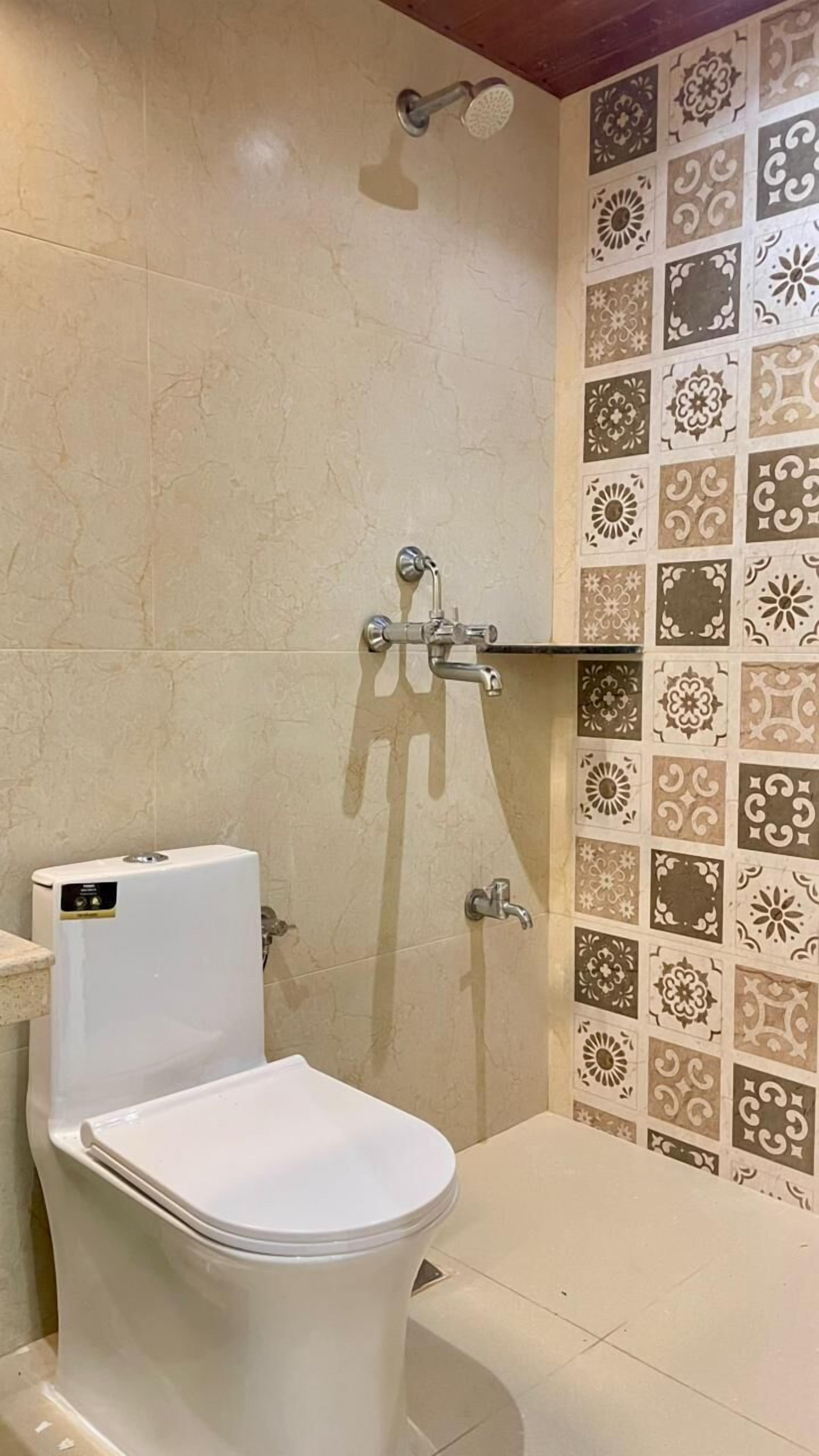 A bathroom with a toilet, a shower, and a tiled wall with decorative patterns.