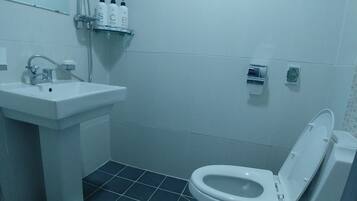 A bathroom with a white sink, a toilet, and a shower. There are slippers on the floor.