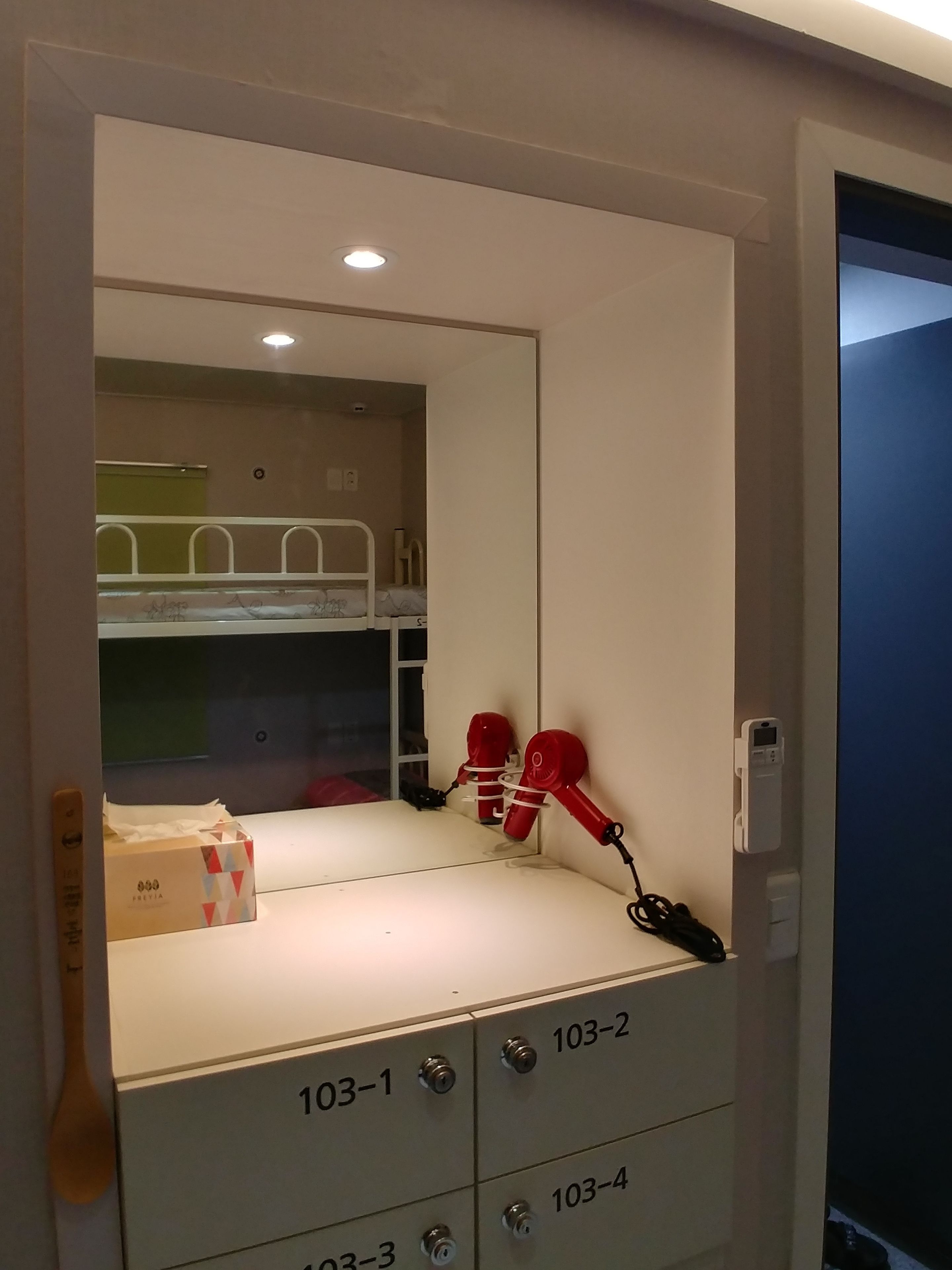 A hotel room with a bunk bed, a mirror, and a set of drawers labeled 103-1 to 103-4.