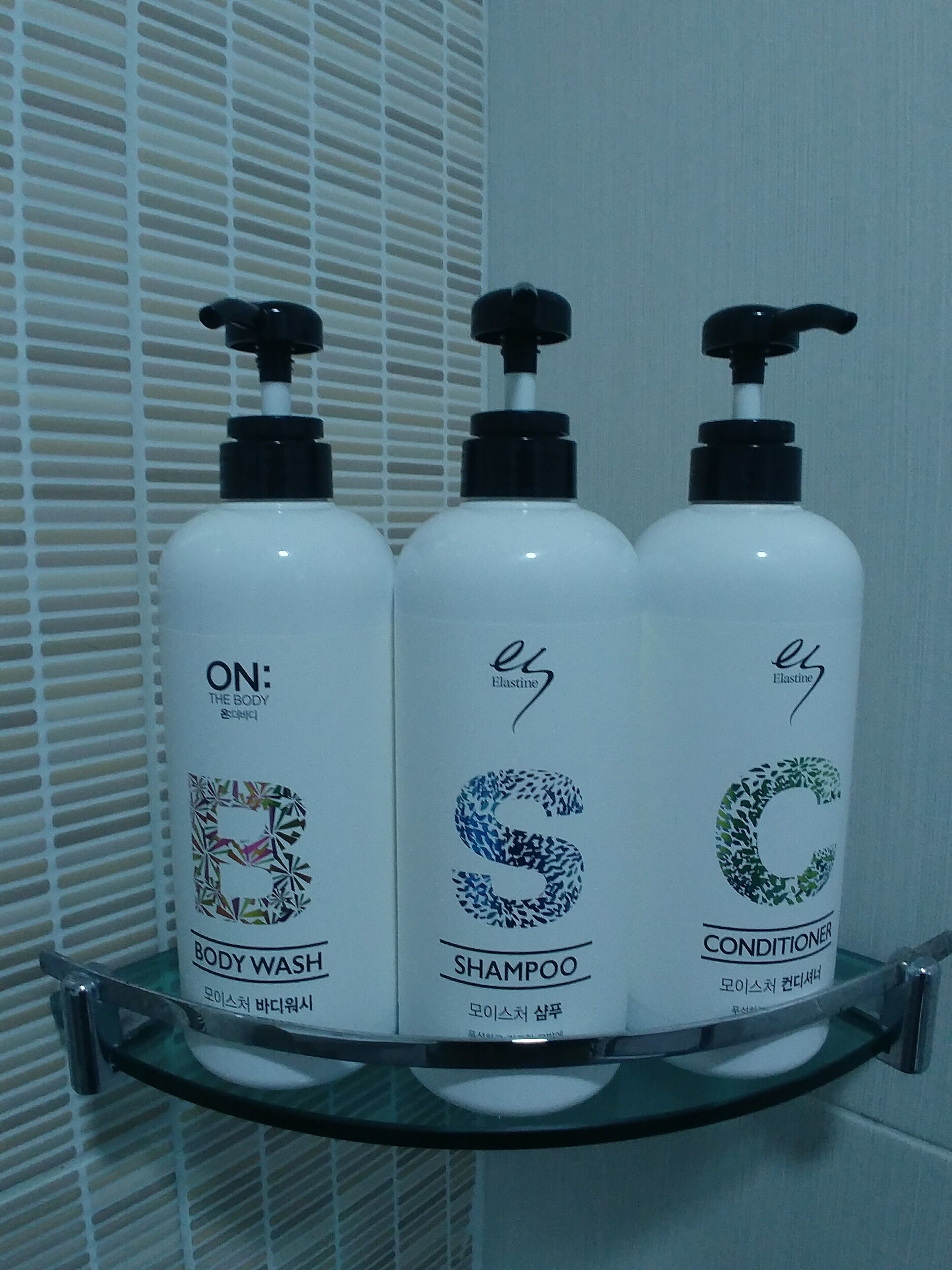 Three bottles of Elastine body wash, shampoo, and conditioner on a glass shelf.