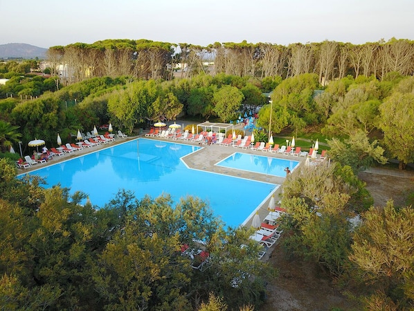 Una amplia piscina al aire libre rodeada de sillas de descanso y sombrillas, con árboles y colinas al fondo.