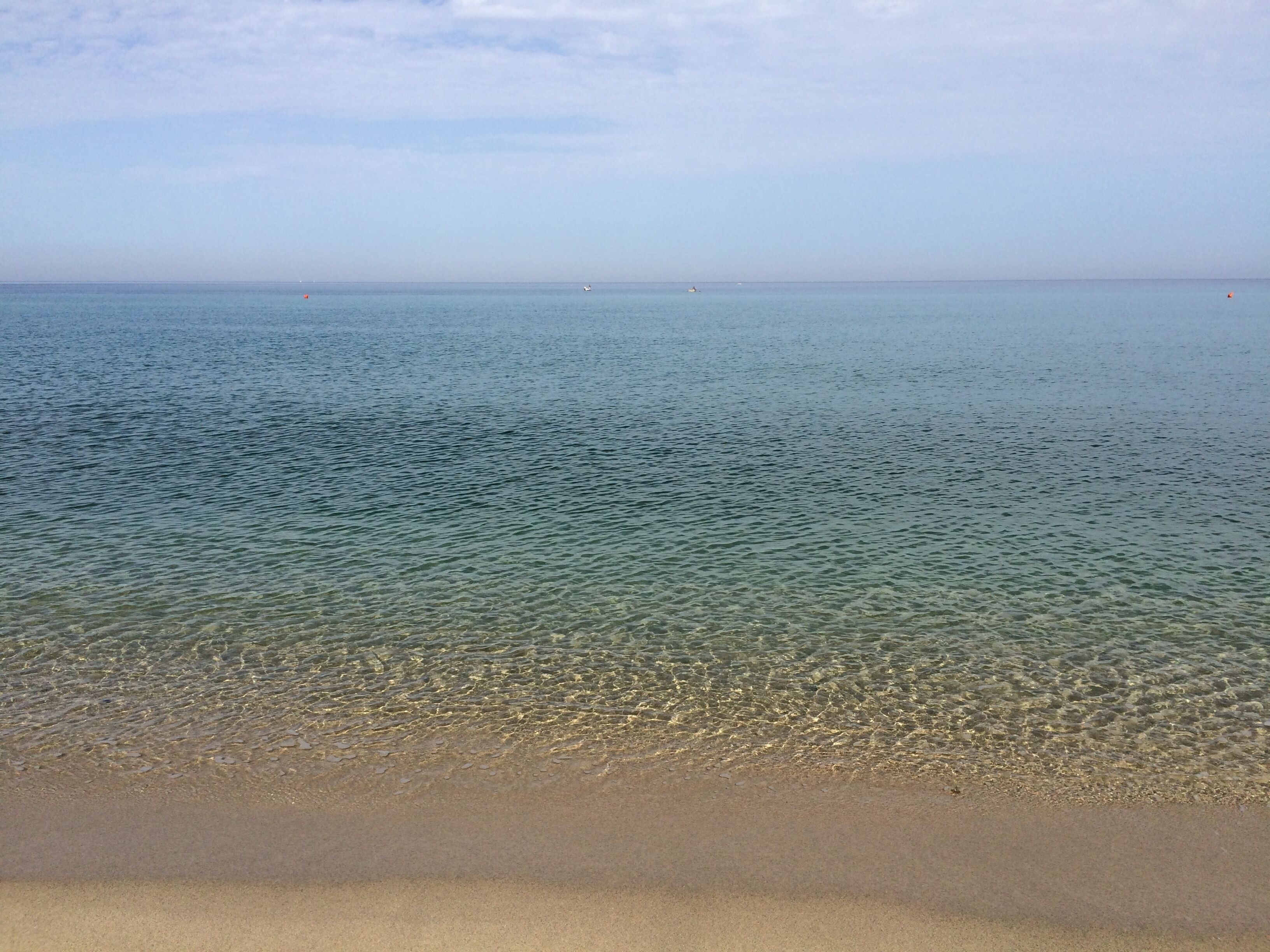 Ein Strand mit klarem, flachen Wasser und sandigem Ufer.