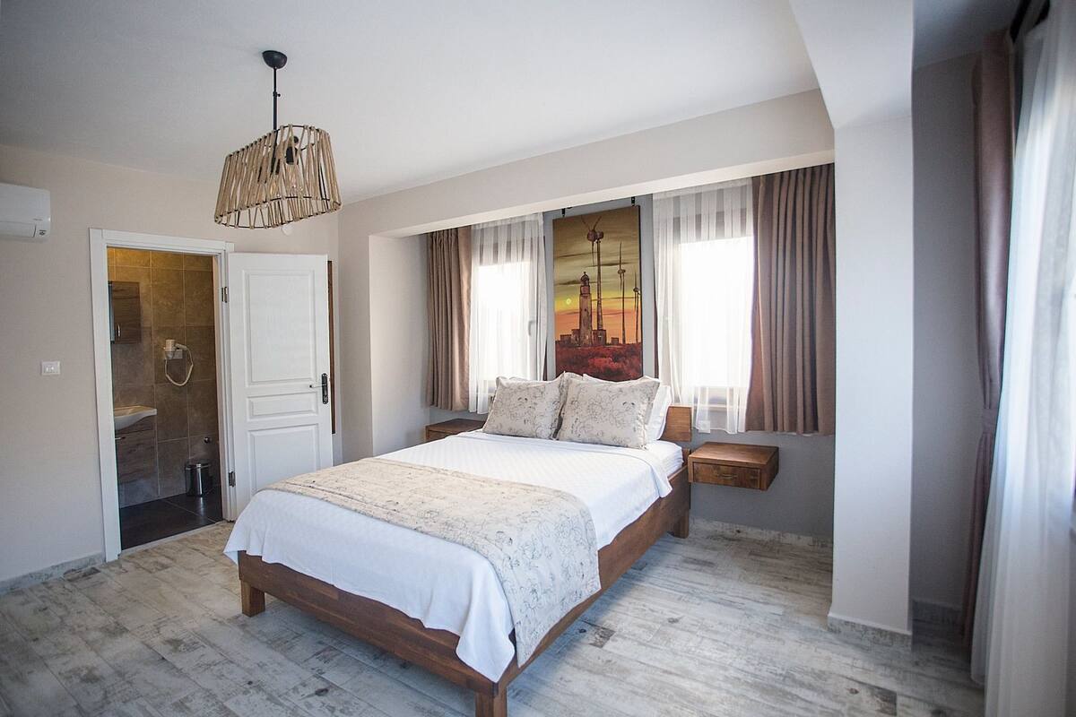 A bedroom with a wooden bed, a hanging light fixture, a window with curtains, and a view of a sunset.