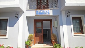 L’entrée d’un hôtel, avec une porte en bois, des plantes en pot et une enseigne indiquant « Hôtel Tenedion ».