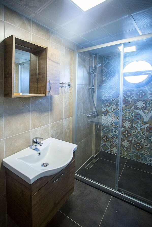 Un baño moderno con un lavabo grande, un mueble de madera y una ducha con azulejos estampados.