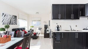 Una cucina moderna con mobili neri e una zona pranzo con tavolo in vetro e cuscini rossi.