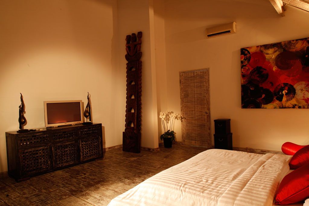 A bedroom with a bed, a dresser, a television, a decorative pillar, a wall-mounted artwork, and a potted plant.