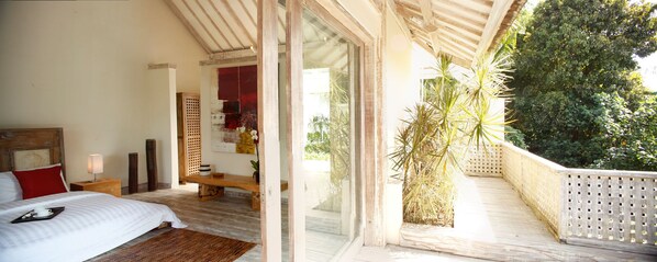 A bedroom with a bed, bedside table, lamp, and a view of the balcony. - Villa Infinity Bali (Canggu)