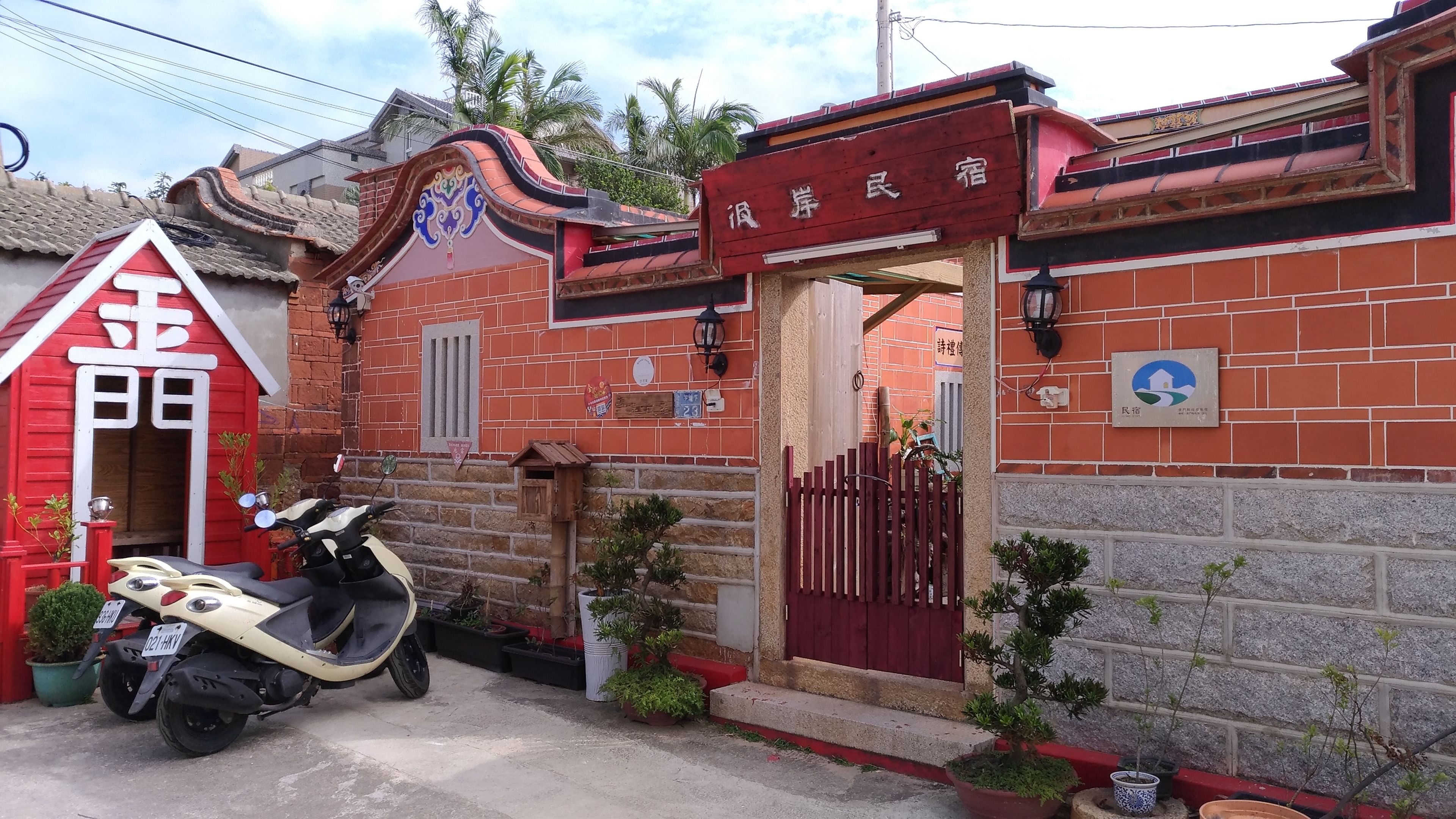 A traditional building with a red entrance, a scooter parked in front, and a small garden area.