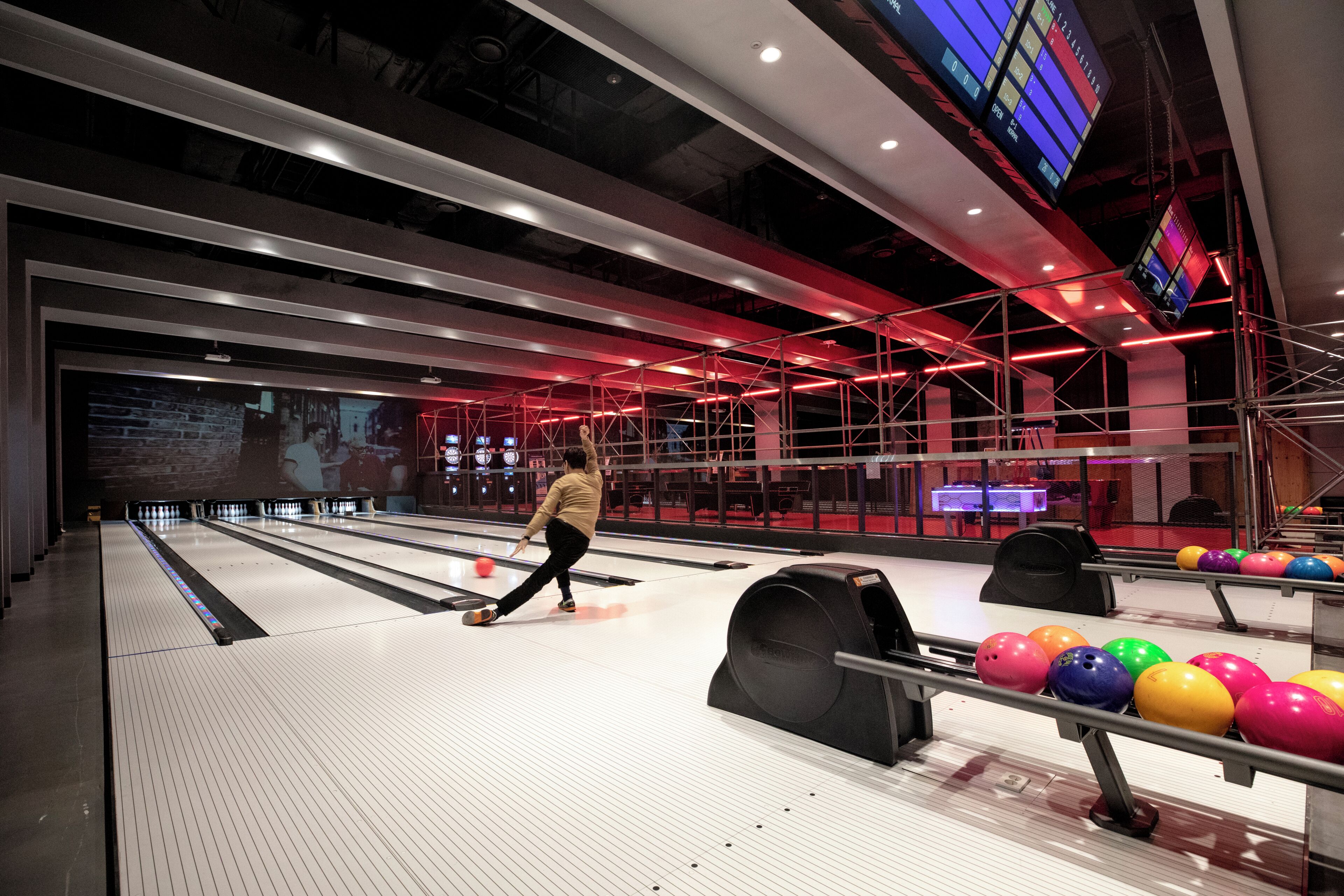 A bowling alley with multiple lanes, a person bowling, and colorful bowling balls.