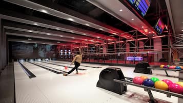 Una bolera con múltiples pistas, una persona lanzando bolos y coloridas bolas de boliche.