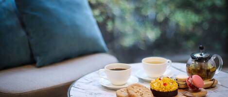 Un coin salon accueillant avec une table préparée pour le thé, comprenant une tasse, une soucoupe, une théière, des biscuits et un macaron.