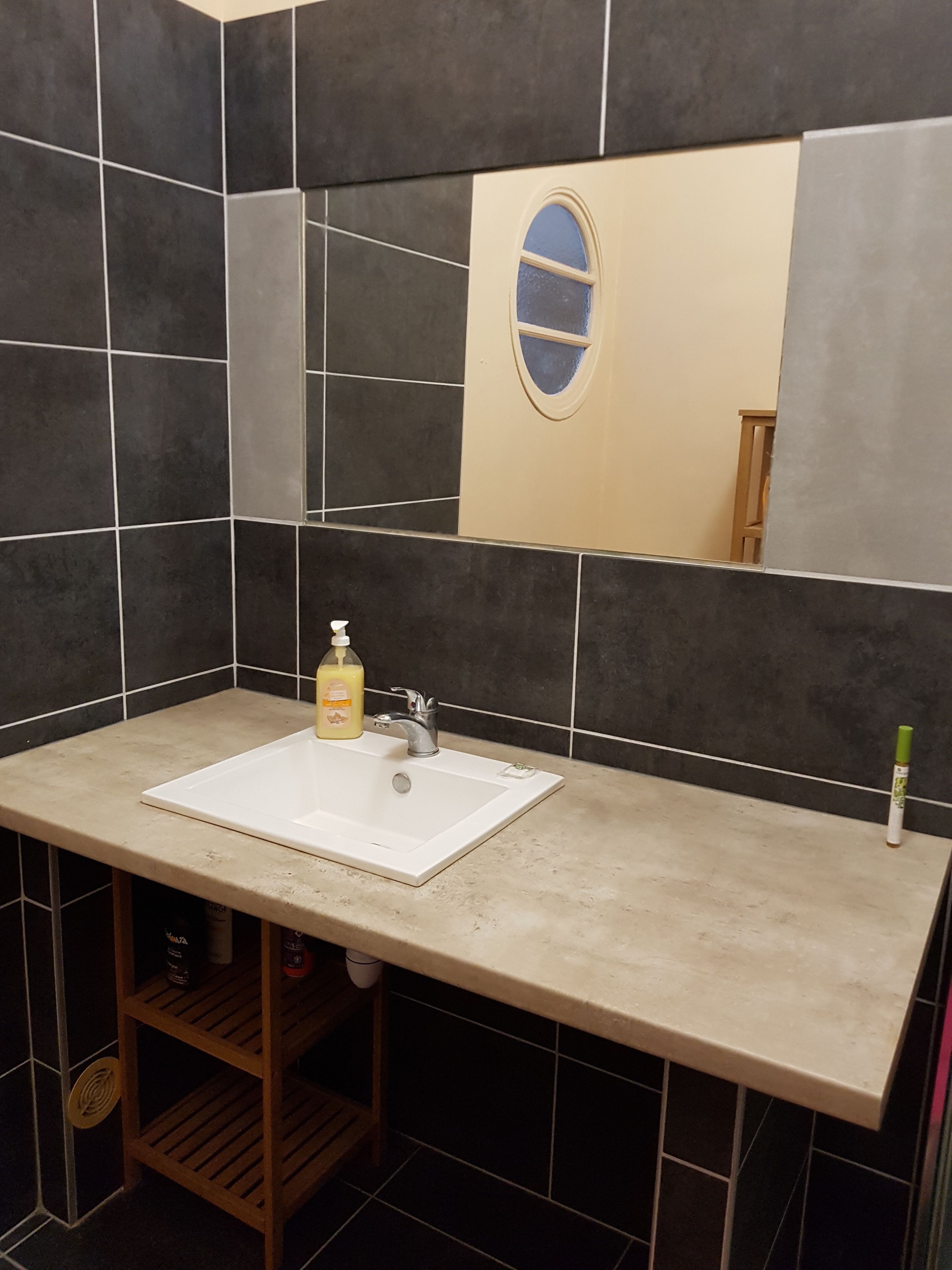 Een badkamer met een wit wastafel, donker betegelde wanden en een spiegel boven het wastafel.