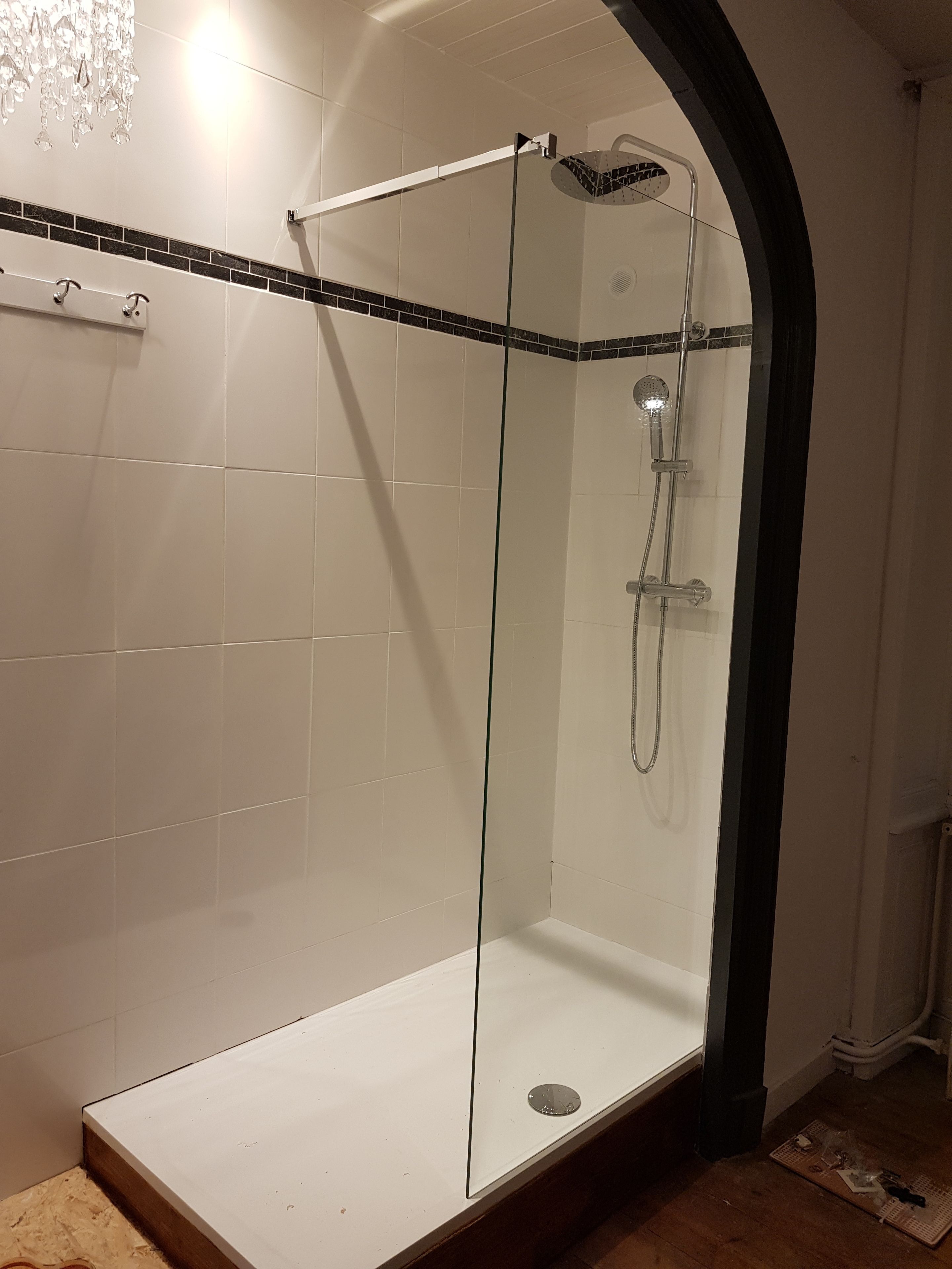A glass-enclosed shower with a tiled floor and a black arch.