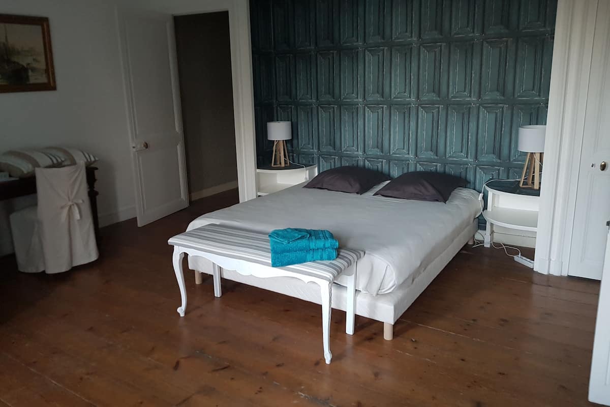 Ein Schlafzimmer mit einem Bett, Nachttischen, einem Sessel und einer Tür.