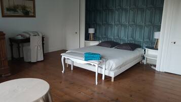 Un dormitorio con cama, mesitas de noche, una silla, una mesa y un cuadro en la pared.