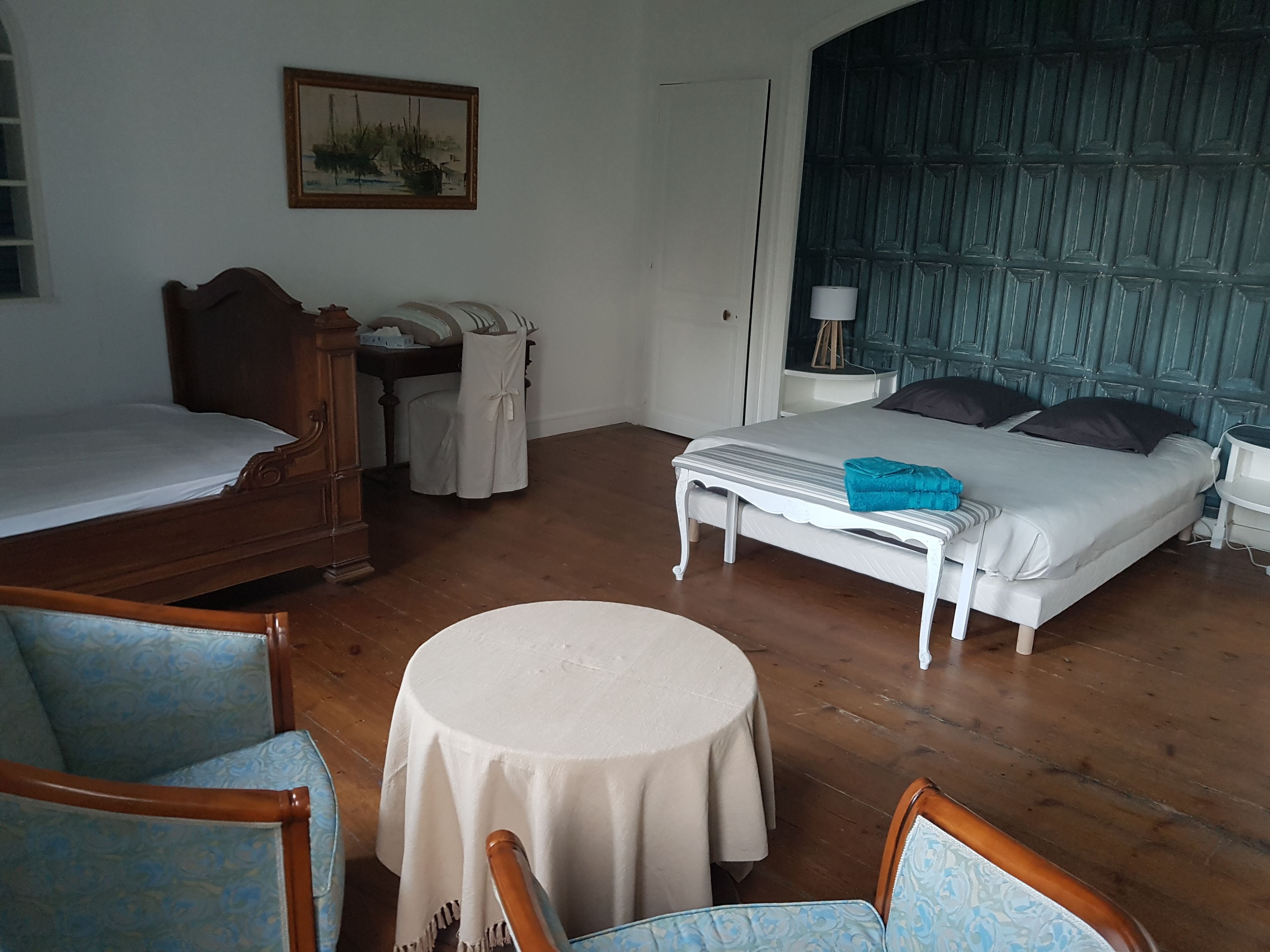 A room with a bed, a chair, a table, and a painting on the wall.