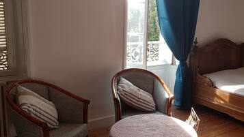 Una habitación con una cama, una silla, una mesa y un ventanal con cortinas.