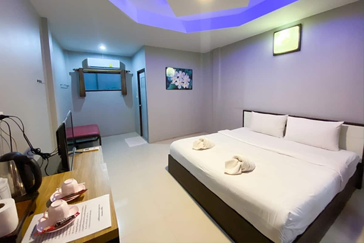 A hotel room with a large bed, a desk with a chair, a small table with cups and a menu, and a wall-mounted air conditioner.