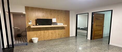 Une chambre d’hôtel moderne avec un comptoir d’accueil en bois, un téléviseur à écran plat et une petite poubelle.