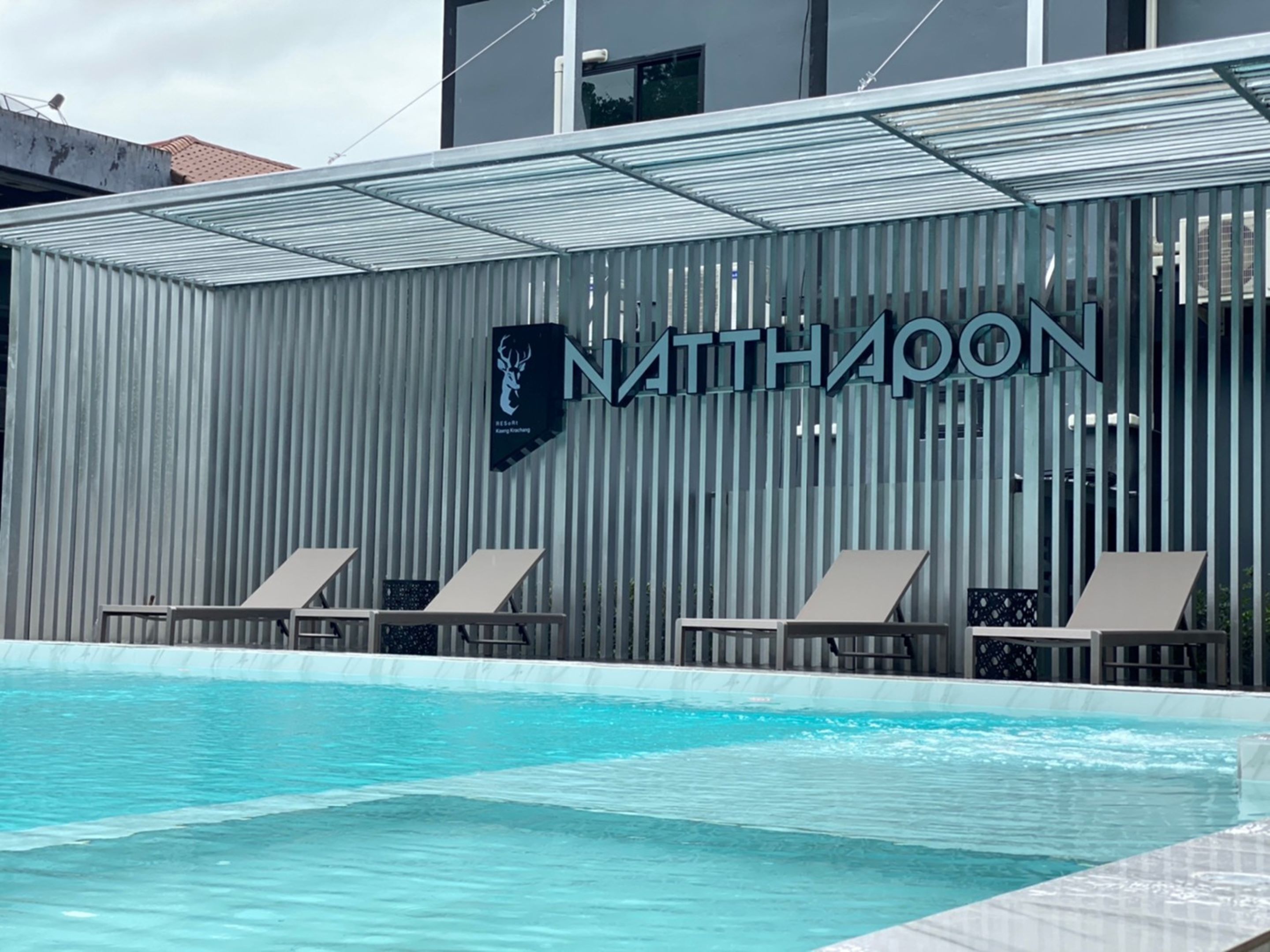 Un hotel moderno con piscina, un cartel grande que dice "NATTHAPON" y dos sillones de piscina.