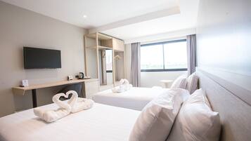 A hotel room with two beds, a flat-screen TV, a mirror, a desk, and a window with curtains.