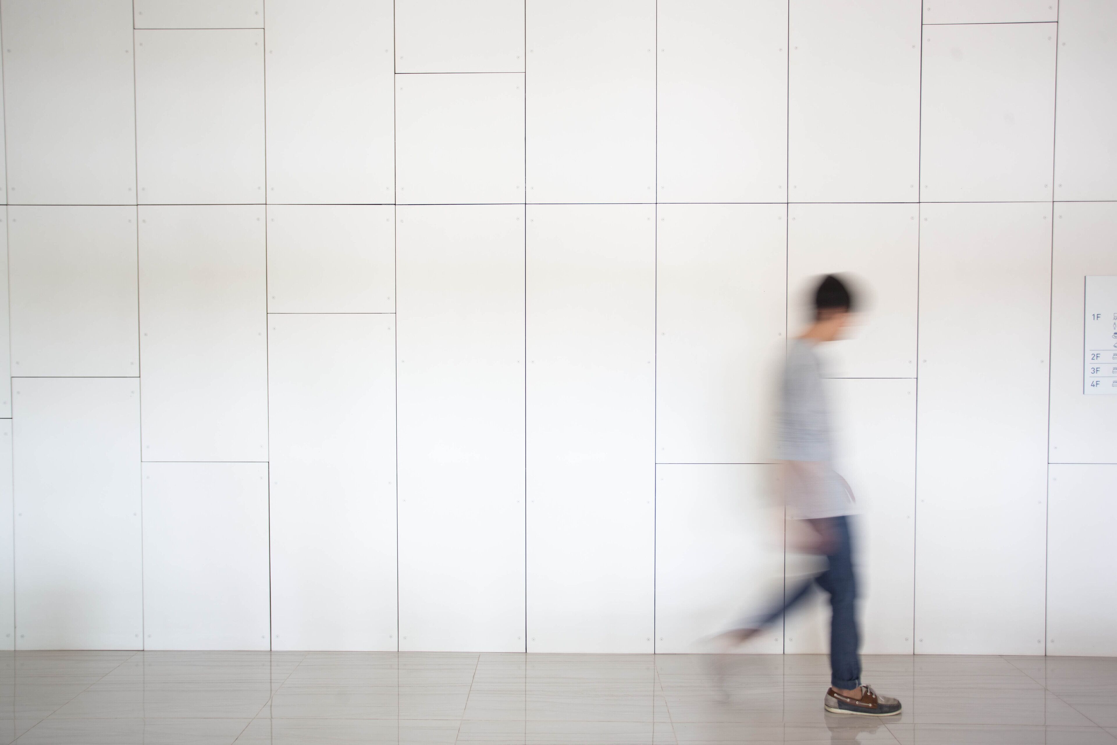A person walking in a hallway with white walls and a tiled floor.