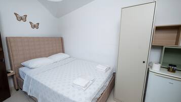 Ein Schlafzimmer mit einem Bett, Kissen, einem Kleiderschrank und einem kleinen Schrank mit Toilettenpapierhalter.