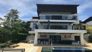 Ein modernes, zweistöckiges Haus mit Schwimmbad, Sitzgelegenheit im Freien und einem Balkon.