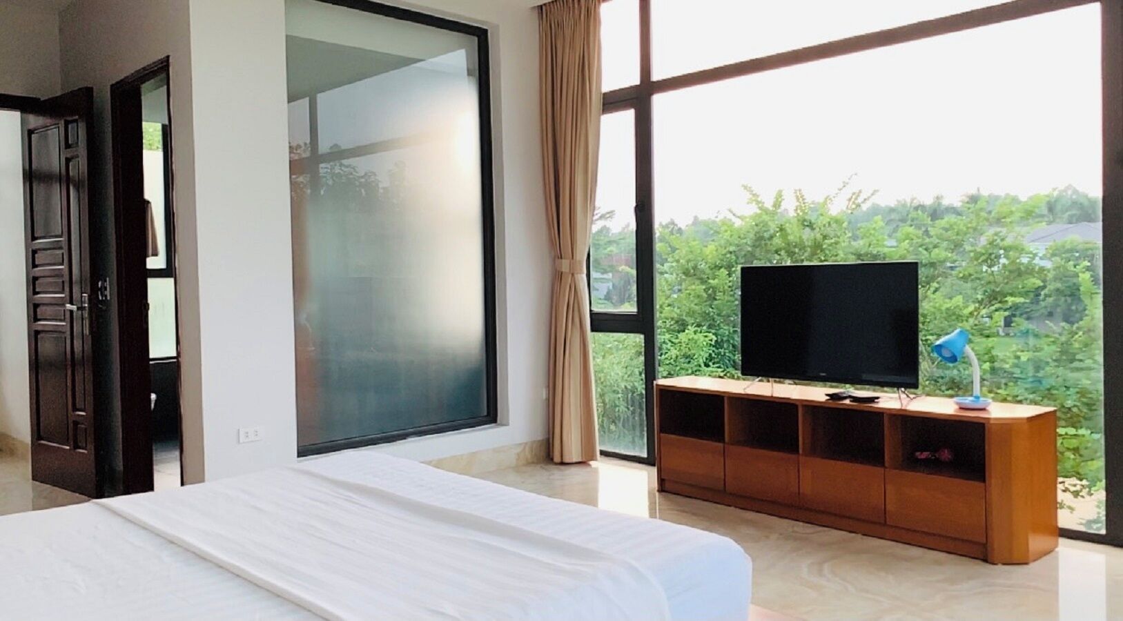 Habitación de hotel con una cama grande, un televisor sobre un soporte de madera y vistas al exterior.