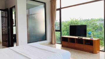 Habitación de hotel con una cama grande, un televisor sobre un soporte de madera y vistas al exterior.