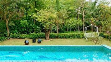 A swimming pool with a tiled edge, surrounded by lush greenery and a small garden area with a swing set.