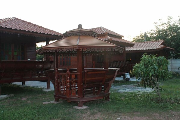 A traditional wooden gazebo with a tiled roof, surrounded by a grassy area and a small tree. - Baanpoonana (Na Yai Am)