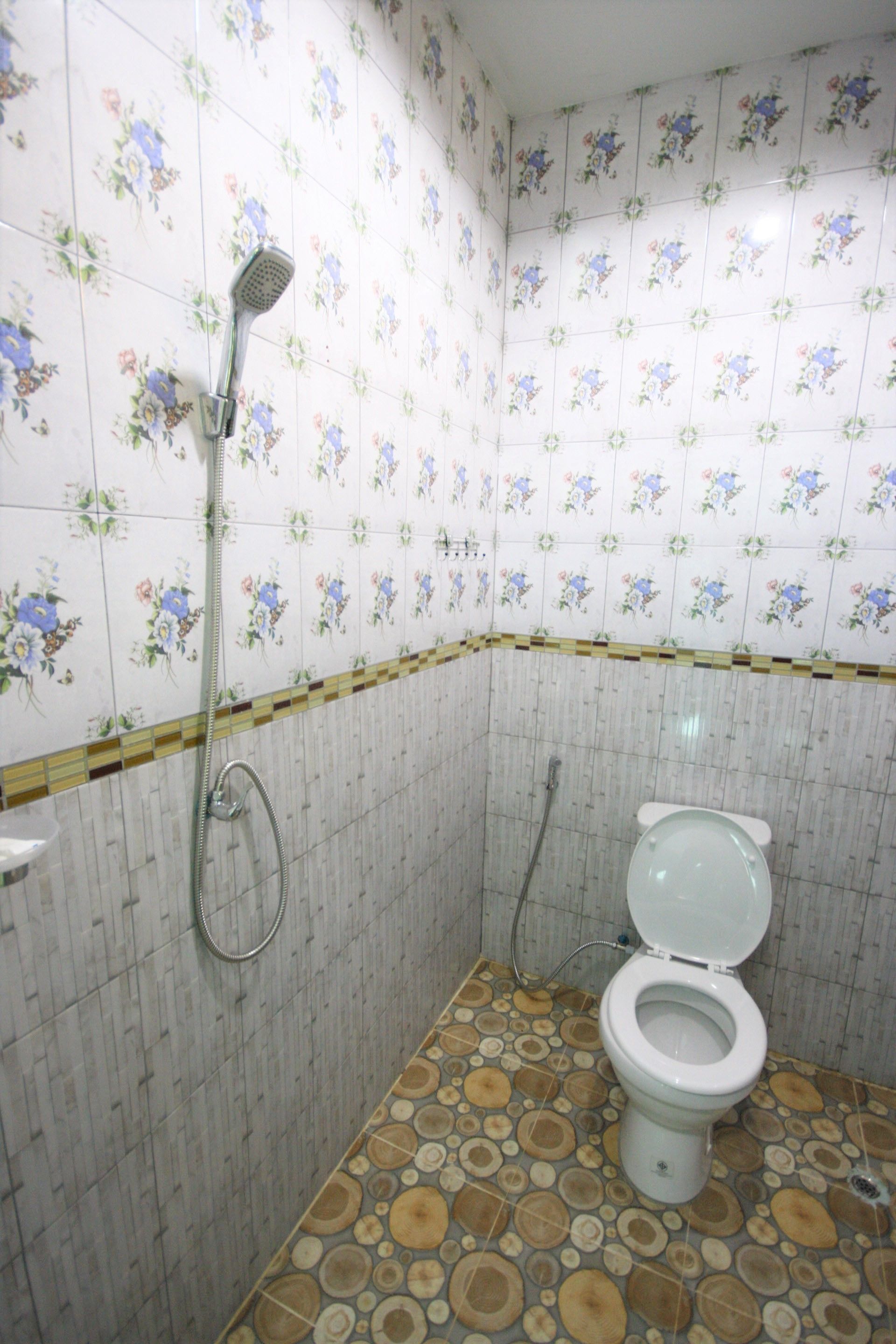 A bathroom with floral patterned tiles, a toilet, and a shower with a handheld showerhead.
