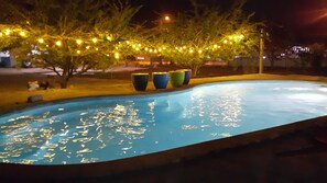 A swimming pool with a curved edge, surrounded by trees and outdoor seating with colorful planters. - Baanpoonana (Na Yai Am)