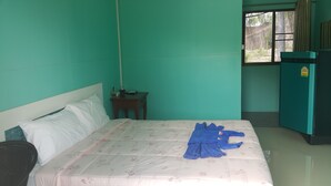 A room with a bed, a small table, a window, and a refrigerator. - Baanpoonana (Na Yai Am)