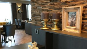 A modern kitchen with a stone wall backsplash, a framed deer picture, and a dining area in the background.