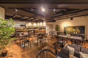 A modern restaurant with wooden flooring, black metal chairs, and a central dining area.