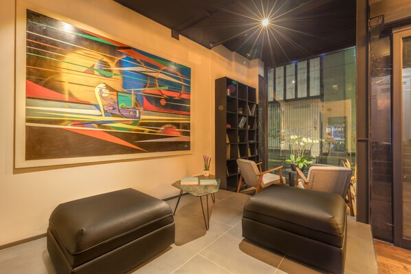 Un salon moderne avec deux canapés en cuir noir, une table basse en verre et un grand tableau abstrait accroché au mur.