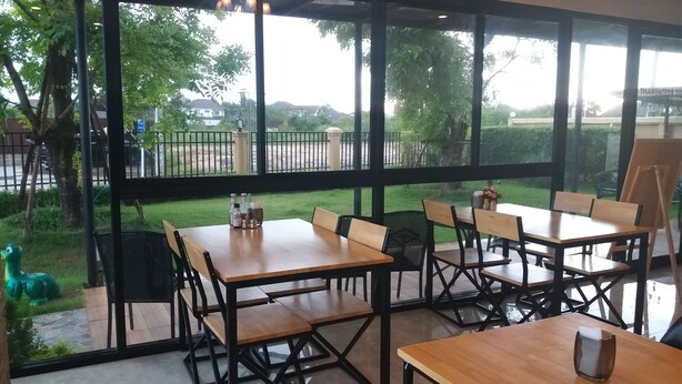 Un restaurante con terraza, grandes ventanales y vistas al entorno verde.
