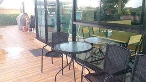 Un patio exterior con paredes de vidrio, mobiliario de mimbre y piso de madera.