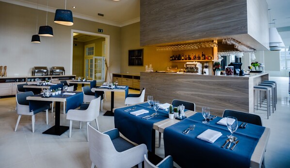 Un restaurant moderne, décoré de bleu et de blanc, avec un bar et une vue sur la cuisine.