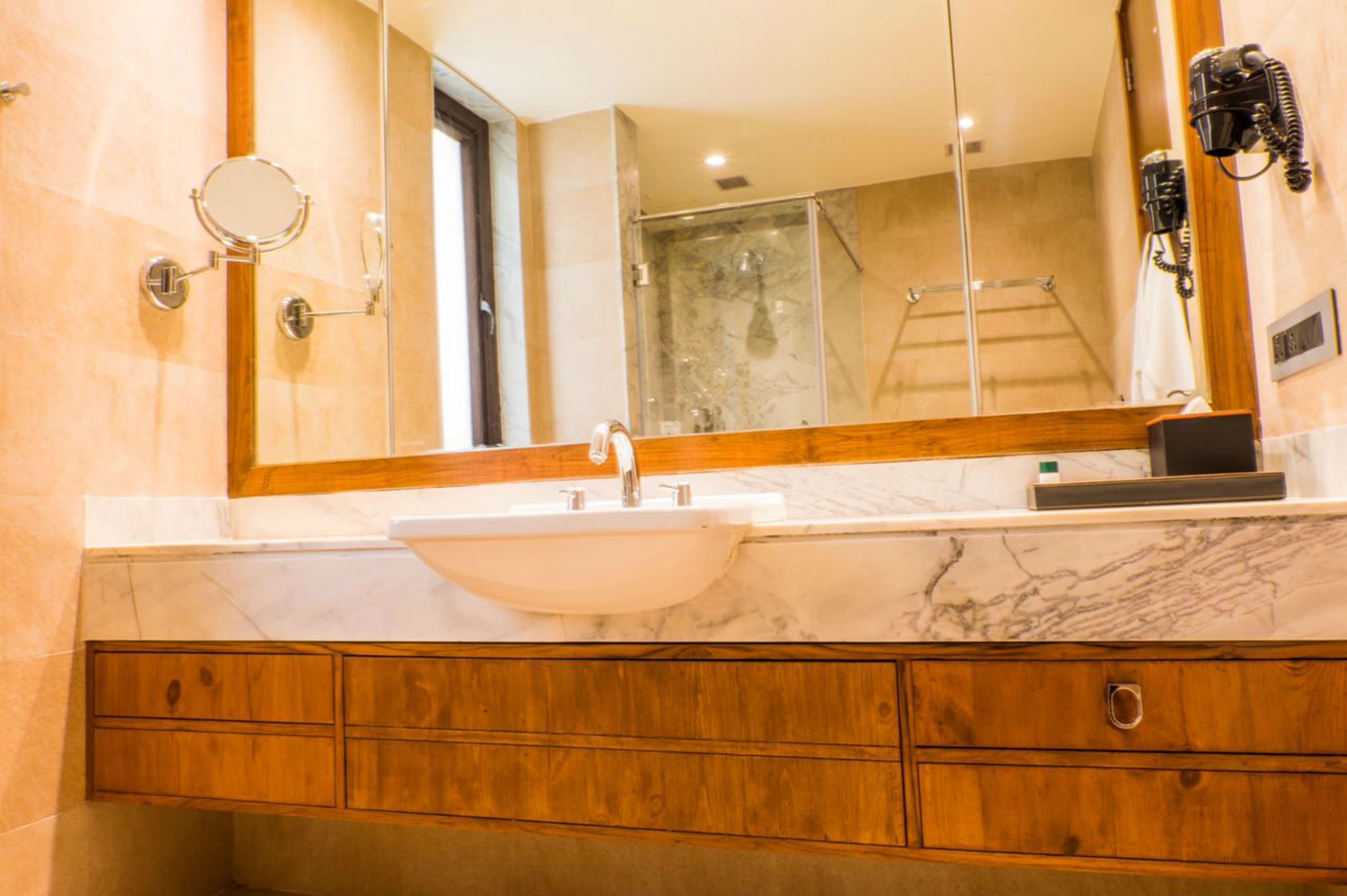 A bathroom with a large mirror, a white sink, wooden vanity, and a glass shower enclosure.
