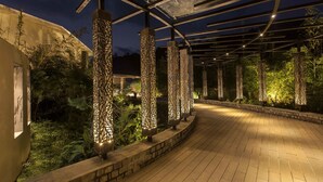 An outdoor walkway with a curved design, surrounded by greenery and decorative lighting fixtures.