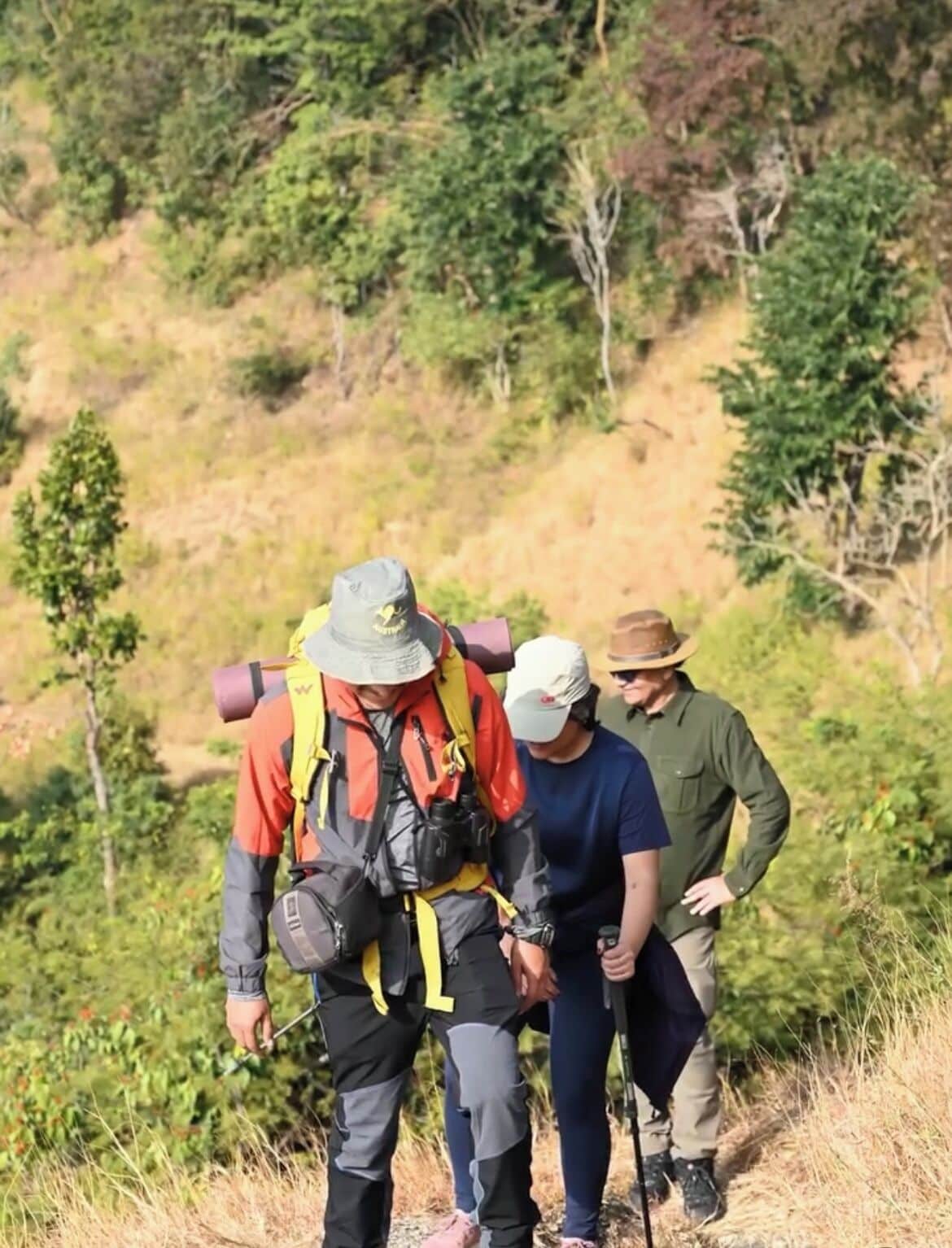Three people hiking in a natural setting with backpacks and hiking poles.