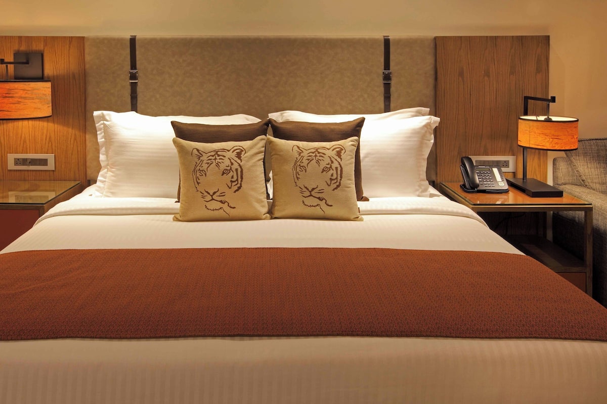 A hotel room with a large bed, two nightstands, a desk, and a lamp.
