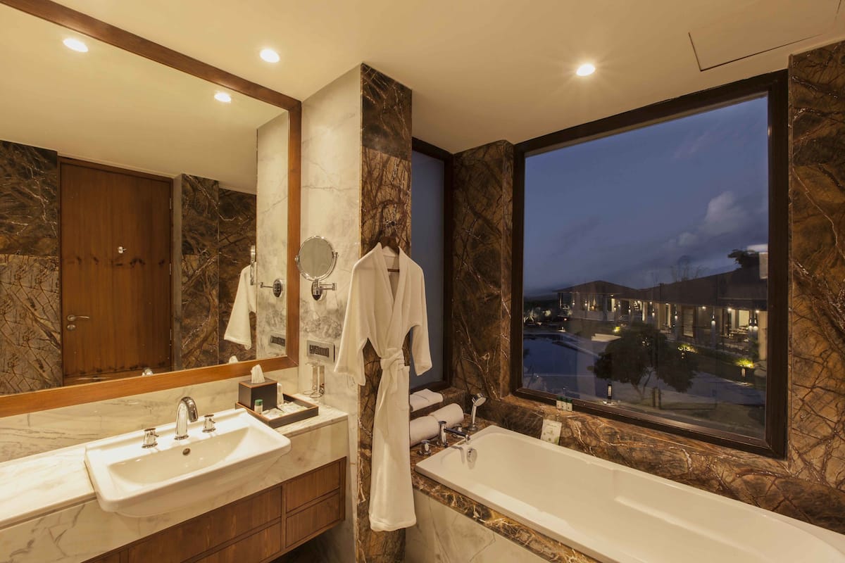 A modern bathroom with a large mirror, two sinks, a bathtub, and a view of a cityscape at dusk.