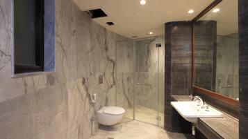 A modern bathroom with a marble floor, a glass-enclosed shower, a white toilet, and a large mirror above the sink.